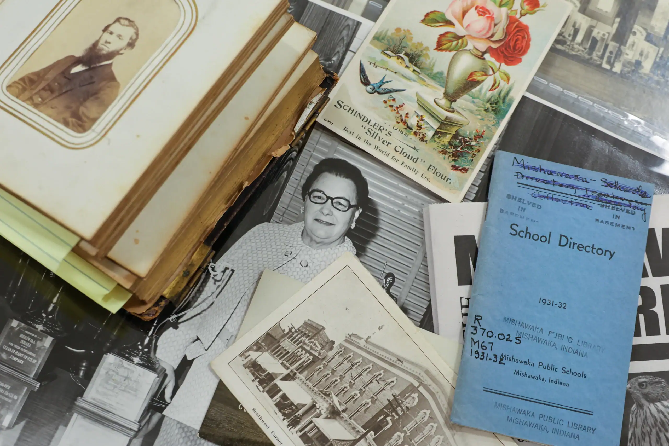 The inside of a glass display case containing various antique photos, art and other printed works related to the city, Mishawaka.