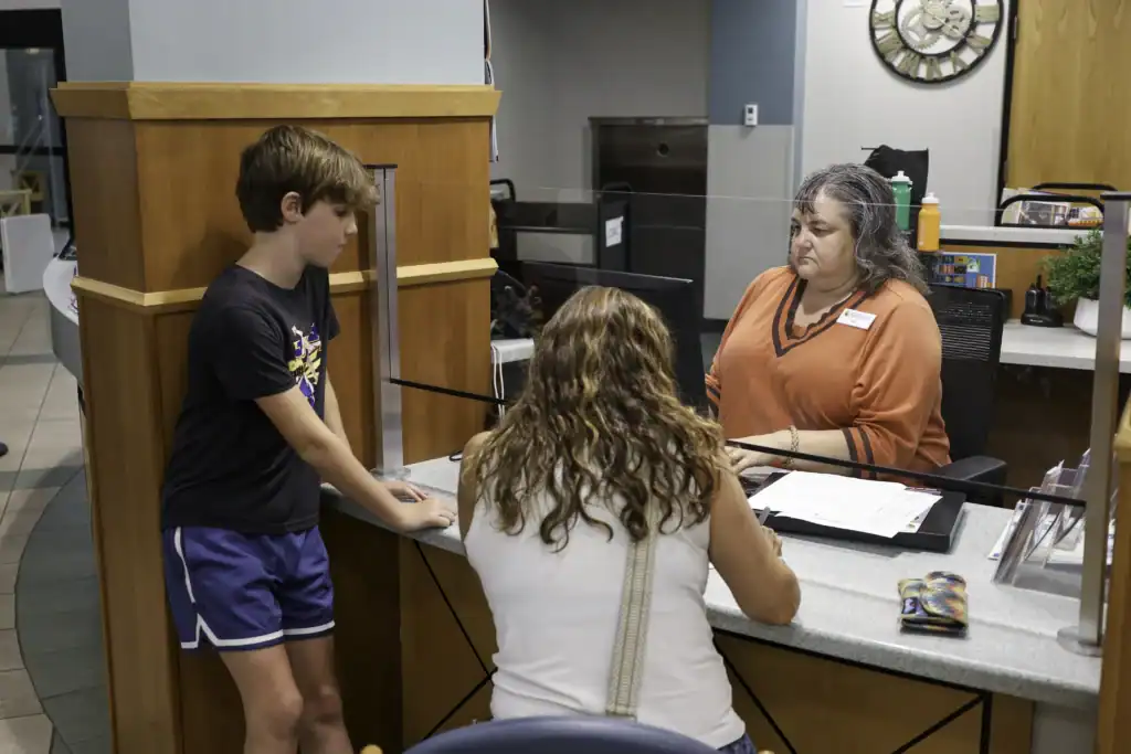 An adult and a youth gather at the Circulation desk while an MPHPL employee creates a library card.